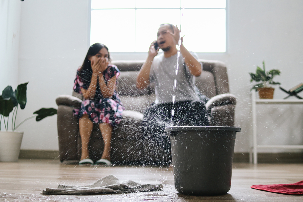 Water damage from roof leak — flooded floor with bucket and burst wall pipes